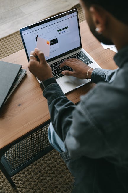 A Person Typing on a Laptop while Holding a Debit Card